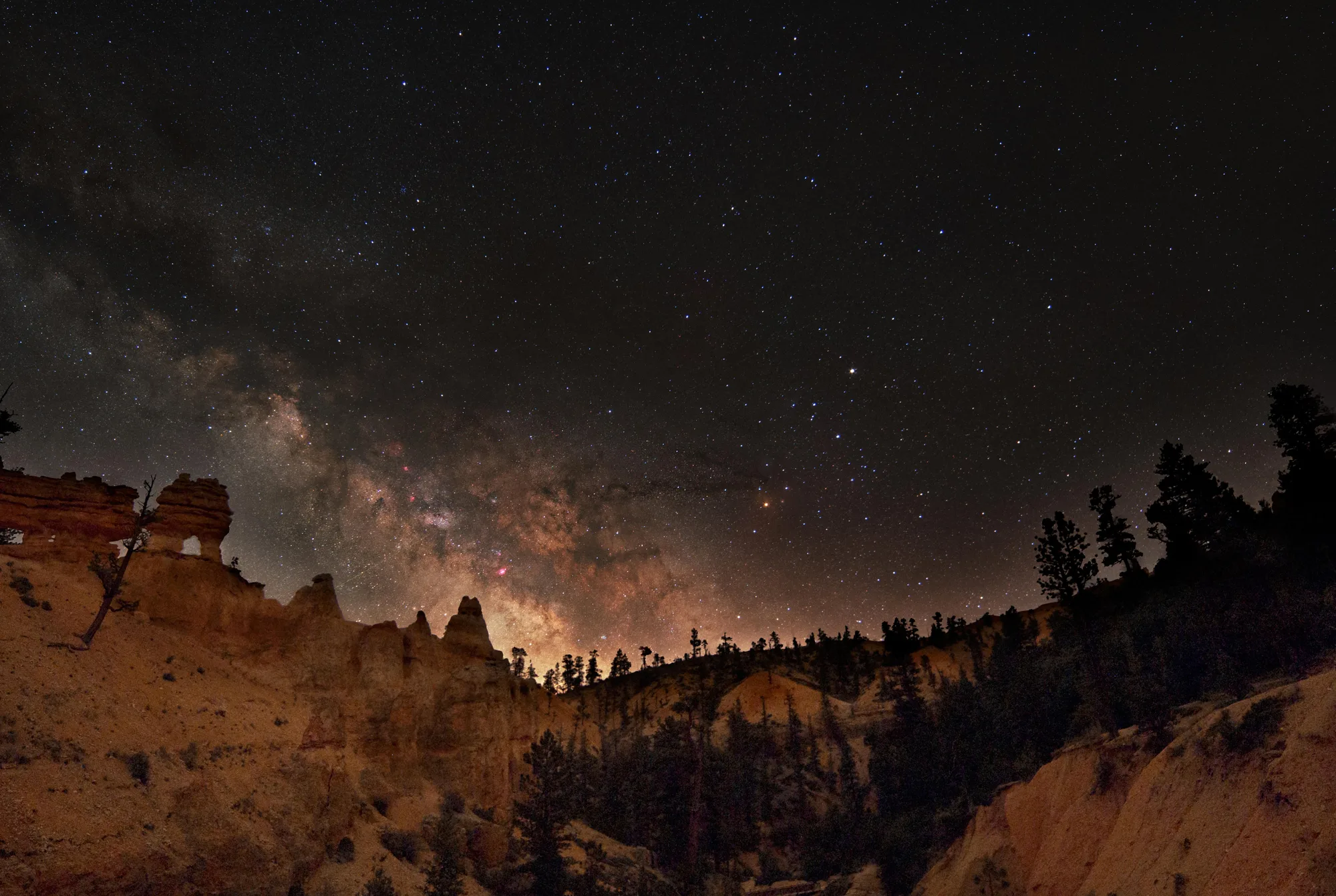 The Milky Way over silhouetted hoodoo spires at Bryce Canyon National Park at night