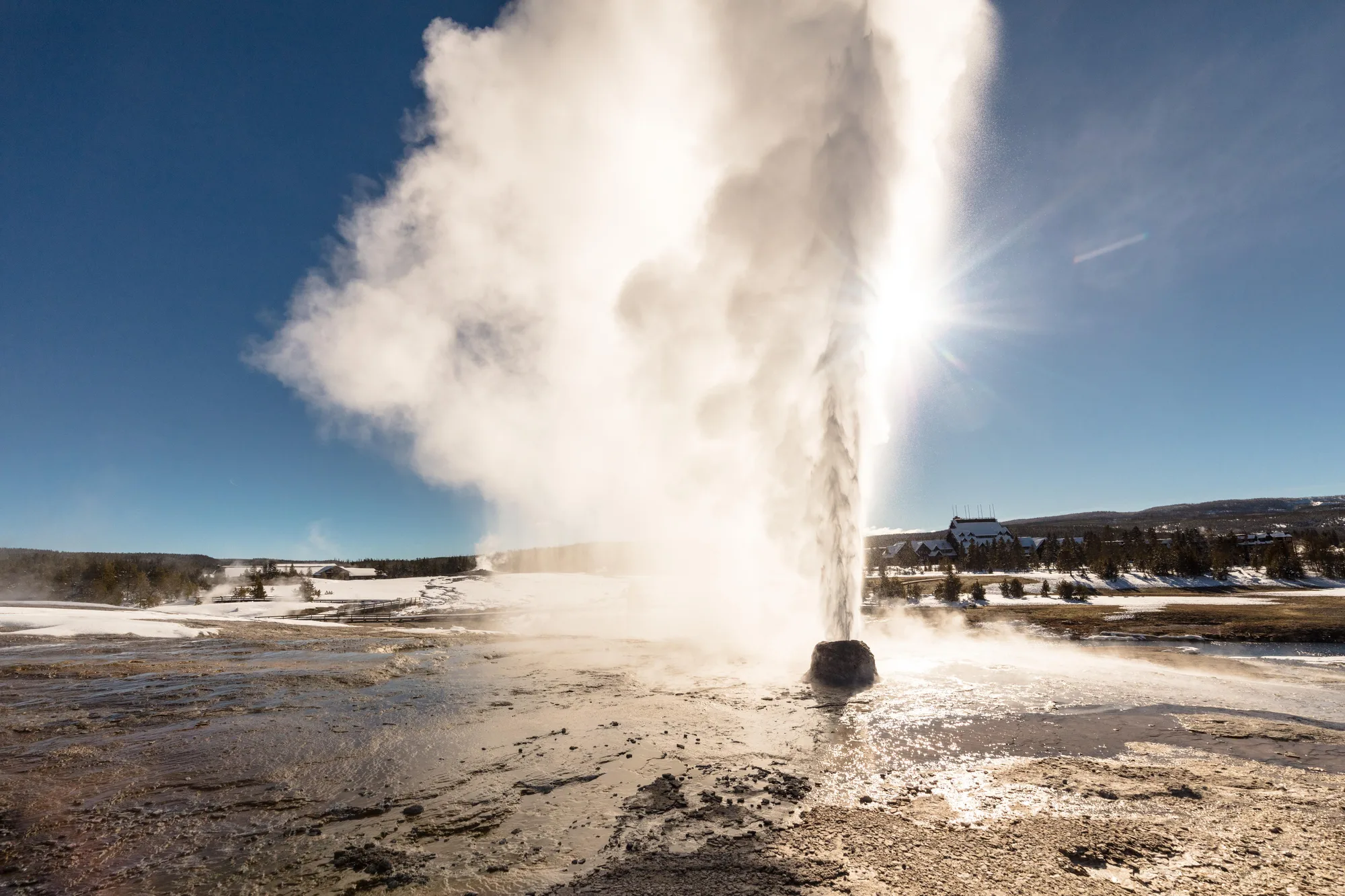 A geyser erupts steam in front of the bright sun in Yellowstone National Park